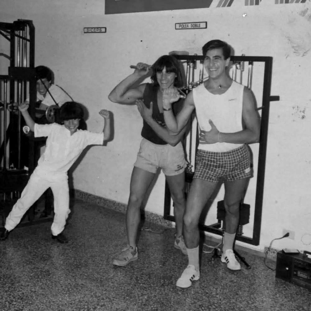 Dos socios haciendo pose de culturismo y un nene imitándolos en la sala de MAB
